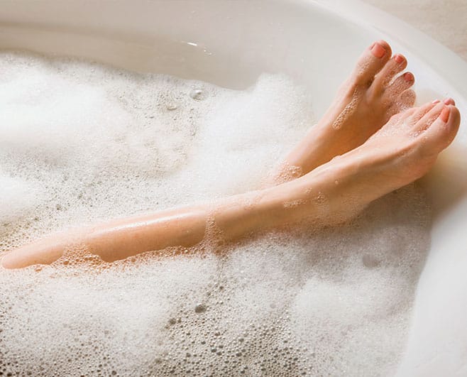 Piernas de una persona relajándose en una bañera llena de espuma, capturando un momento de relajación y cuidado personal