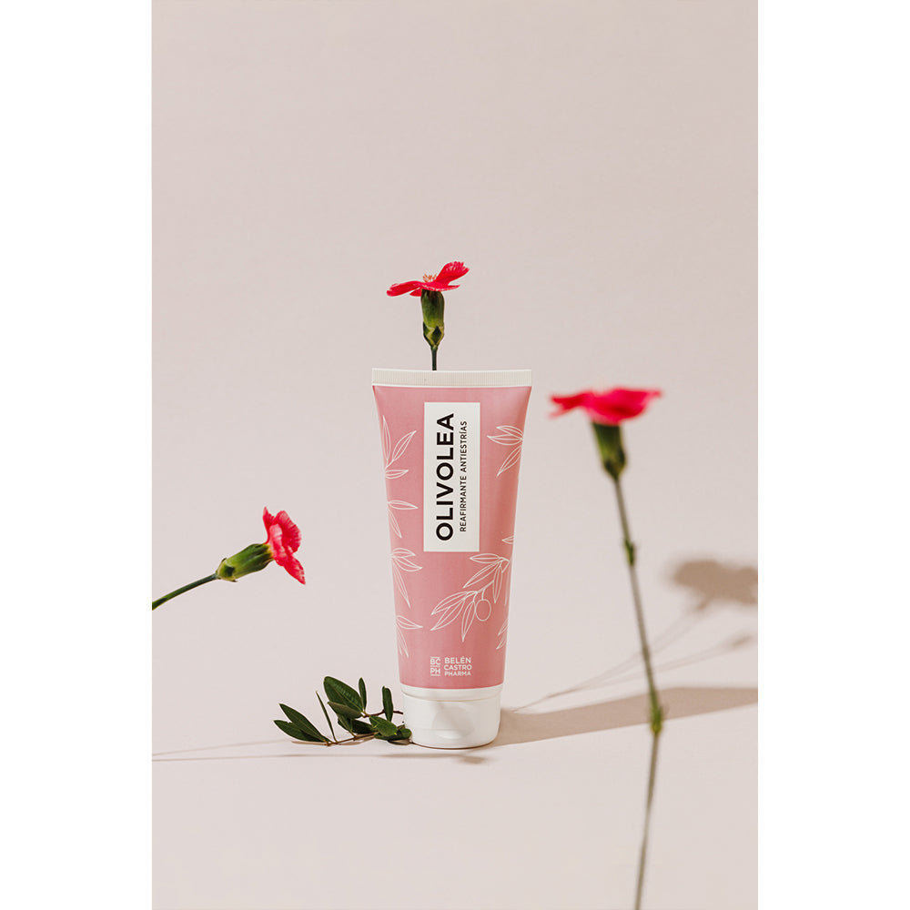 Envase de crema Olivolea reafirmante antiestrías en color rosa rodeado de flores rojas, fondo rosa suave