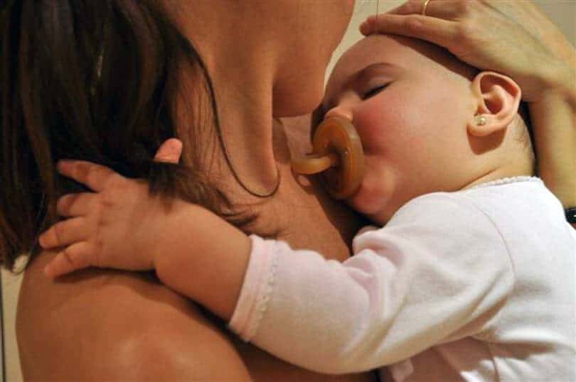 Bebé durmiendo con chupete en brazos de su madre, mostrando cercanía y afecto materno